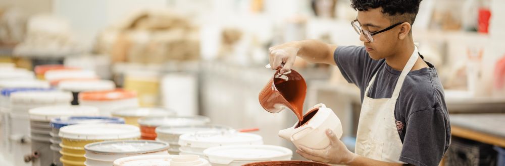 student at The School of Arts and Enterprise tuition-free charter school pouring glaze into a ceramic pot in a pottery studio