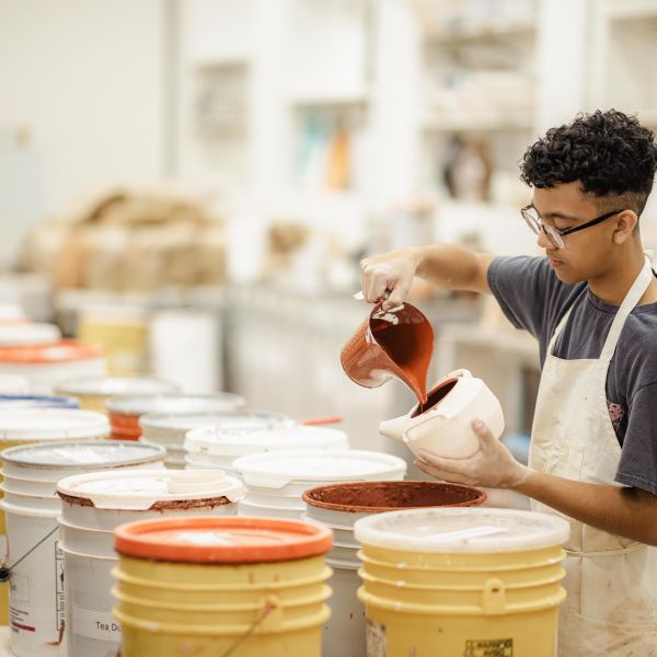 student at The School of Arts and Enterprise tuition-free charter school pouring glaze into a ceramic pot in a pottery studio