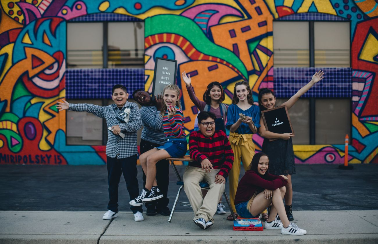 students pose in front of colorful mural outdoors