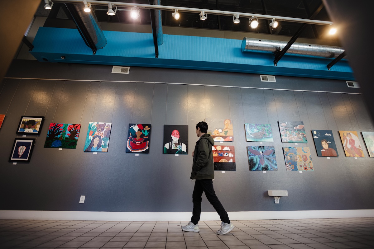 student walks by colorful artwork displayed on a wall