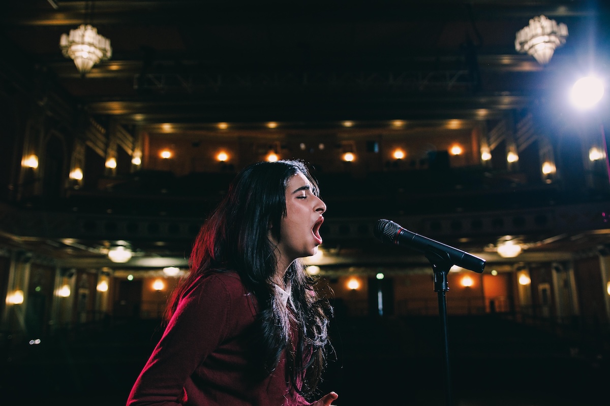 student at The School of Arts + Enterprise charter school singing into a microphone on a stage with lights in the background