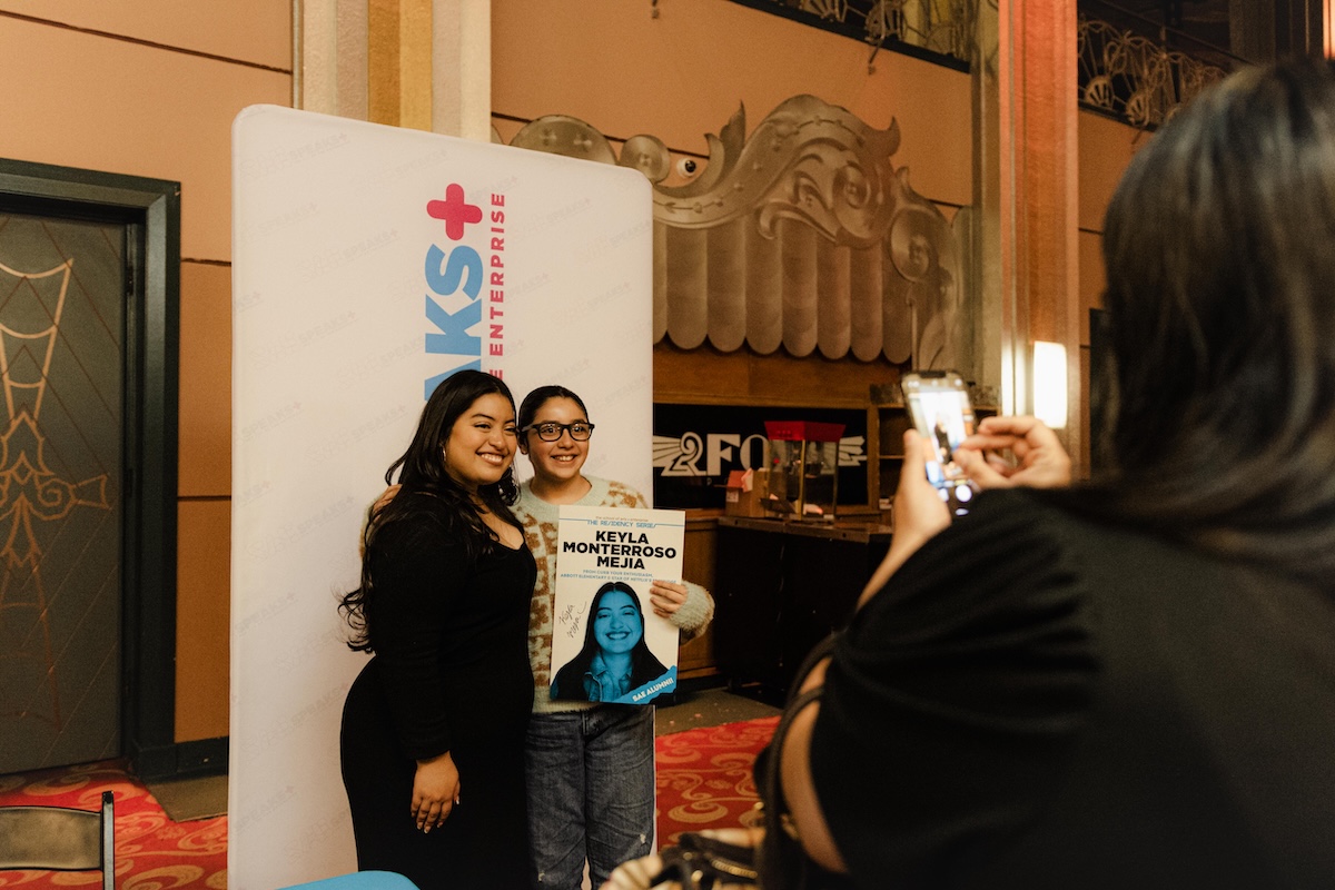The School of Arts and Enterprise tuition-free charter school alumna Keyla Monterroso Mejia smiling with a student for a photo in an auditorium lobby