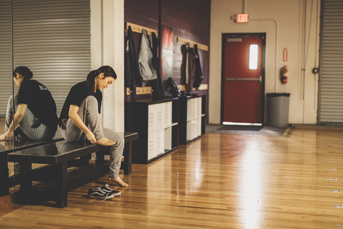 student at tuition-free and audition-free charter middle and high school The SAE putting dance shoes on while seated at the edge of a dance studio