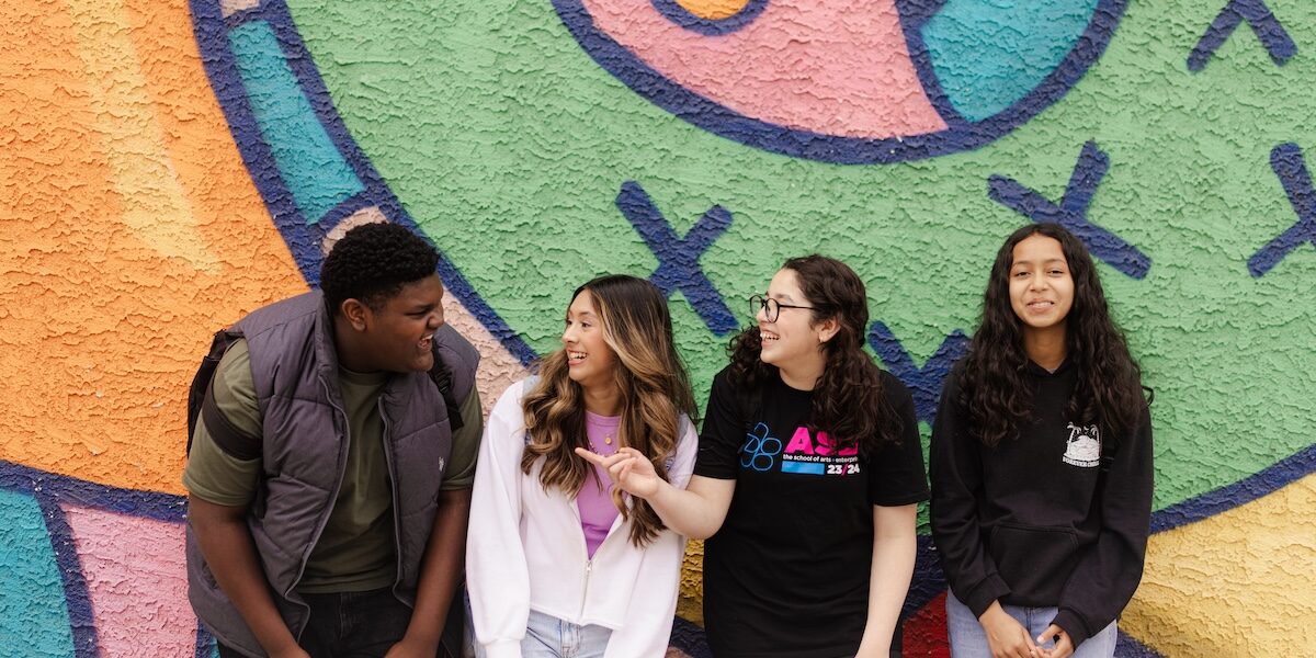 A smiling group of SAE students stands in front of a colorful mural outside.