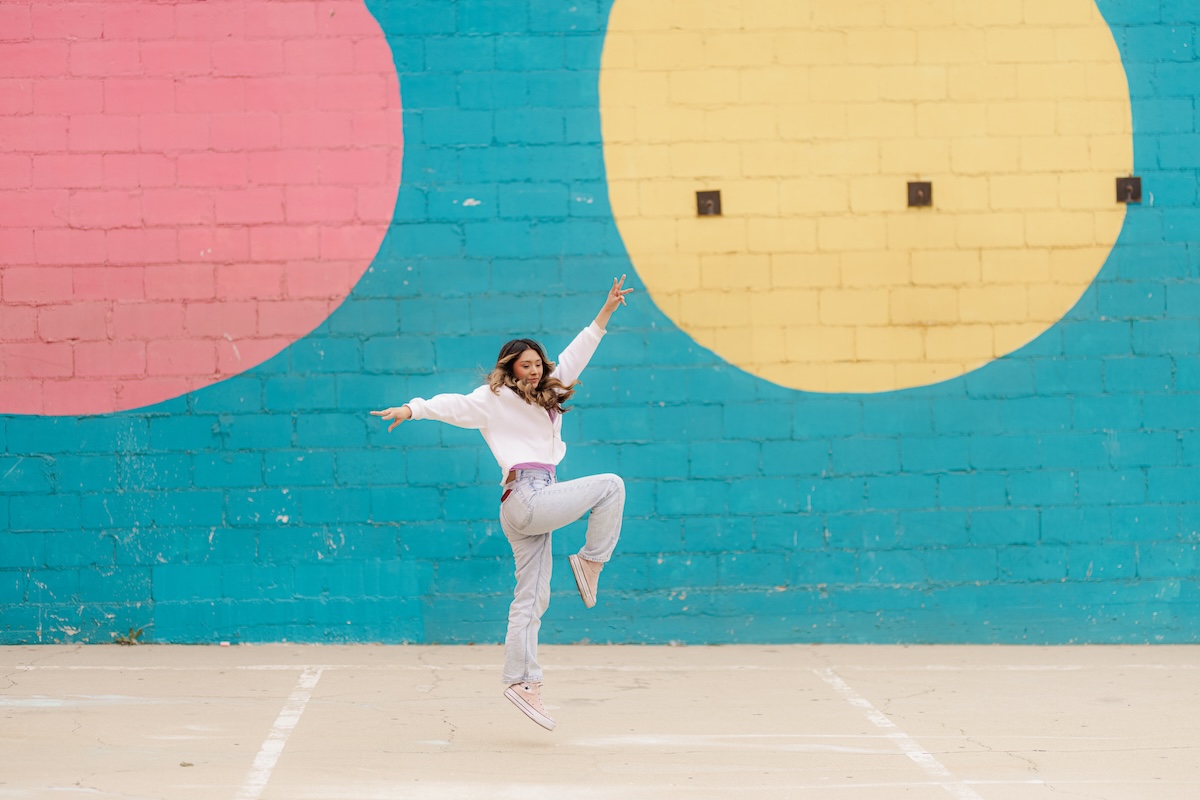 student dances in front of colorful outdoor mural